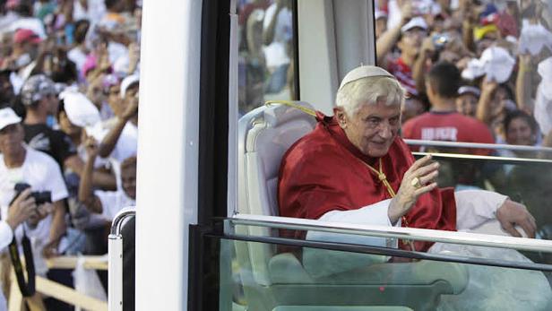 Papst Benedikt XVI. winkt aus einem Papamobil einer Menschenmenge zu.