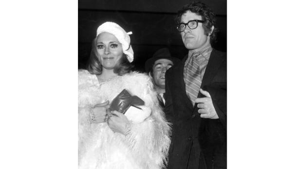 Eine Frau in einem weißen Federkleid und ein Mann mit Brille posieren für ein Schwarzweißfoto.