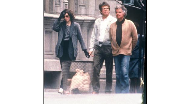 Jacqueline Kennedy Onassis geht mit zwei Männern die Straße entlang.