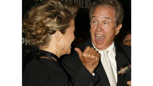 Ein Mann im Anzug gestikuliert aufgeregt, während eine Frau mit Ohrringen daneben steht.