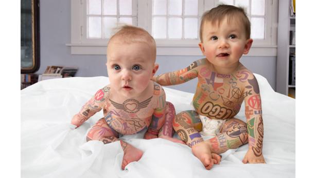 Zwei Babys sitzen auf einem Bett, ihre Körper sind mit verschiedenen Logos und Markennamen „tätowiert“.