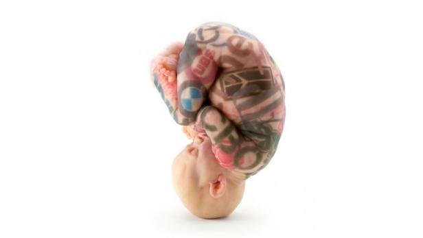 Ein Baby liegt auf dem Kopf, sein Körper ist mit verschiedenen Logos bedeckt.