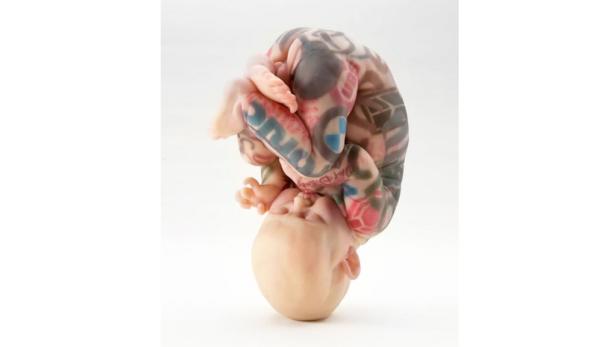 Eine Puppe in Fötusstellung, deren Körper mit Tattoos bedeckt ist.