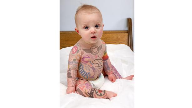 Ein Baby sitzt auf einem Bett und hat viele verschiedene Logos auf seinem Körper tätowiert.