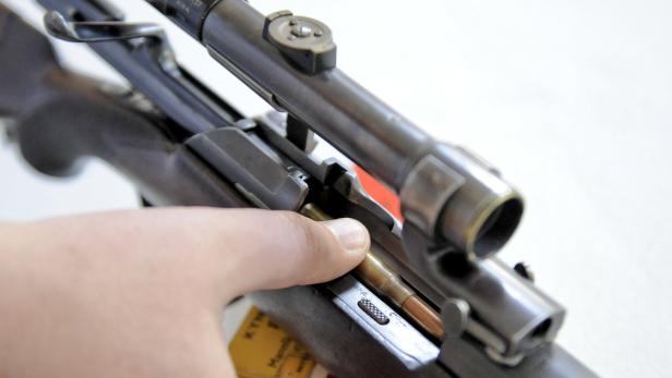 Eine Person führt eine Patrone in ein Gewehr mit Zielfernrohr ein.