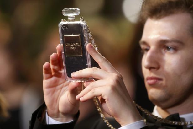 Ein Mann hält ein Smartphone mit einer Chanel-Parfumflakon-Hülle in der Hand.