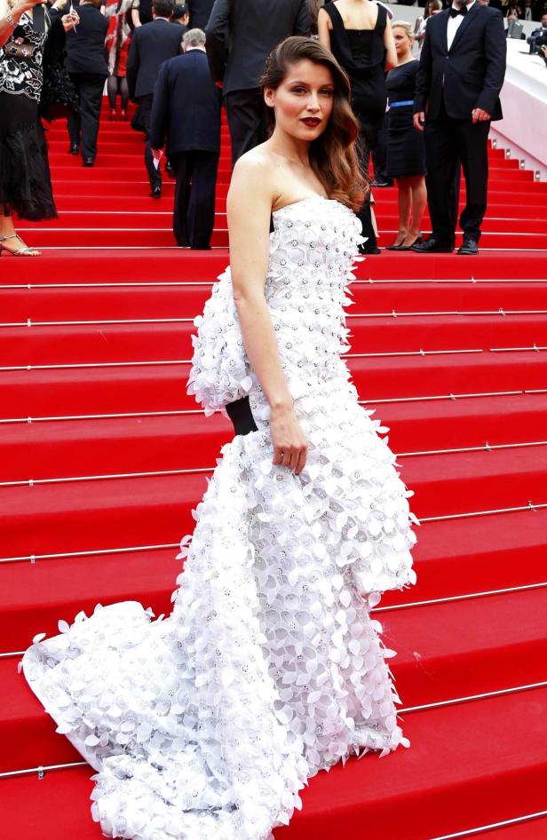 Eine Frau in einem weißen, blumenverzierten Kleid auf einer roten Treppe.