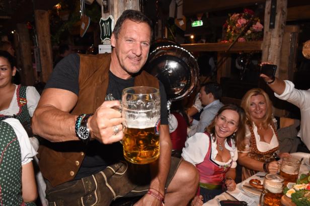 Ein Mann im Lederhosen hält einen Maßkrug Bier in einem Festzelt.