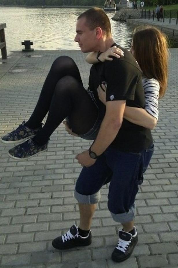 Ein Mann trägt eine Frau Huckepack auf einem gepflasterten Weg am Wasser.