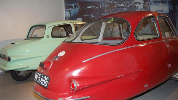 Ein rotes und ein hellgrünes Oldtimer-Auto stehen in einer Ausstellung.