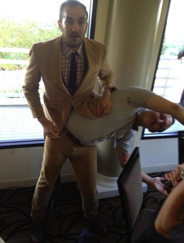 Ein Mann im Anzug trägt einen anderen Mann huckepack.