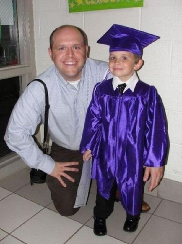 Ein Mann kniet neben einem kleinen Jungen in einem lila Talar und einer Doktorhut zur Abschlussfeier.