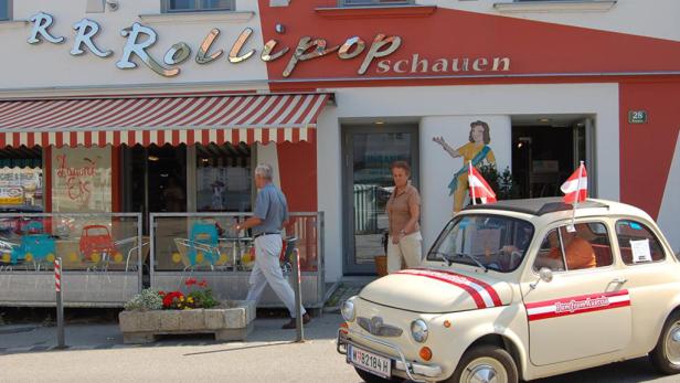 Ein Mann geht vor dem „RRollipop Schauen“-Eiscafé entlang, vor dem ein Fiat 500 mit Österreich-Dekor steht.