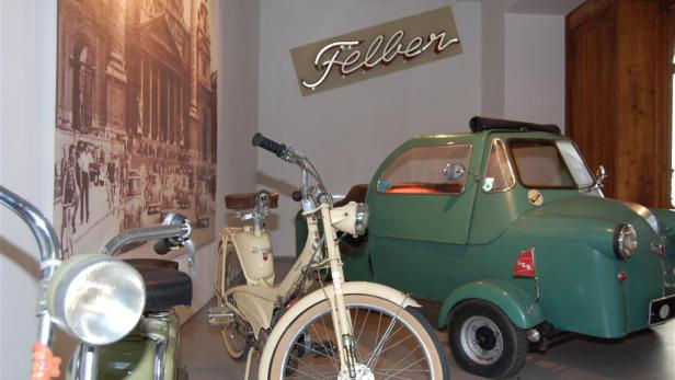 Ein beiges Moped und ein grünes Kleinstauto der Marke Felber stehen in einem Ausstellungsraum.