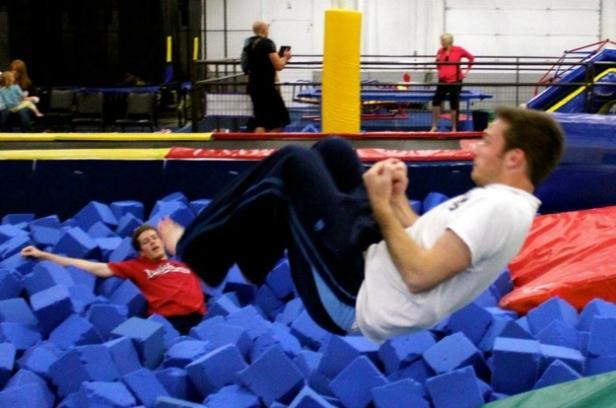 Zwei Männer springen in einem Becken voller blauer Schaumstoffwürfel.