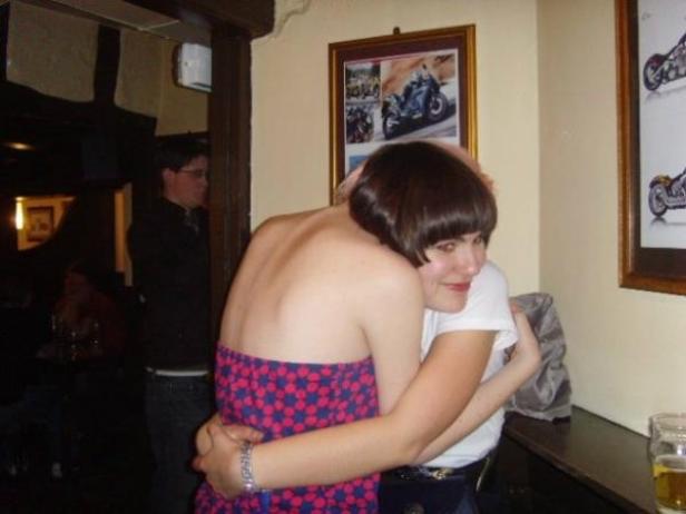 Zwei Frauen umarmen sich in einem Raum mit Motorradbildern an der Wand.