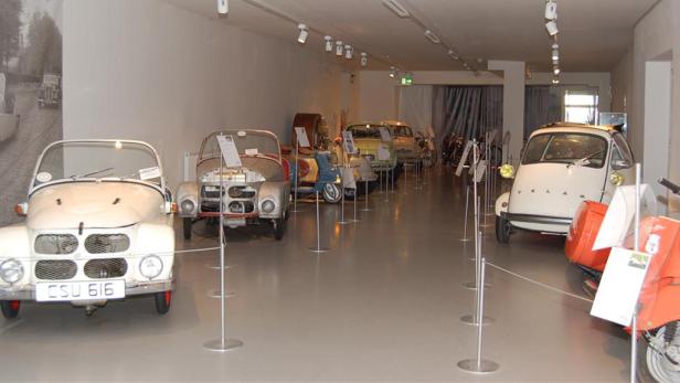 In einem Museum stehen mehrere Oldtimer-Autos und Motorroller.