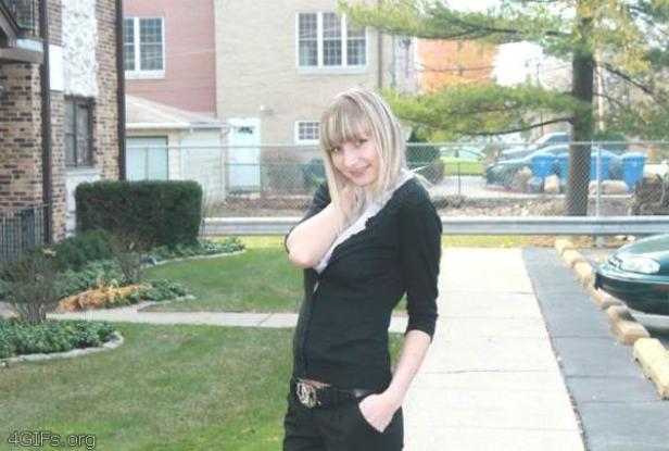 Eine Frau mit blonden Haaren posiert auf einem Gehweg vor einem Wohnhaus.