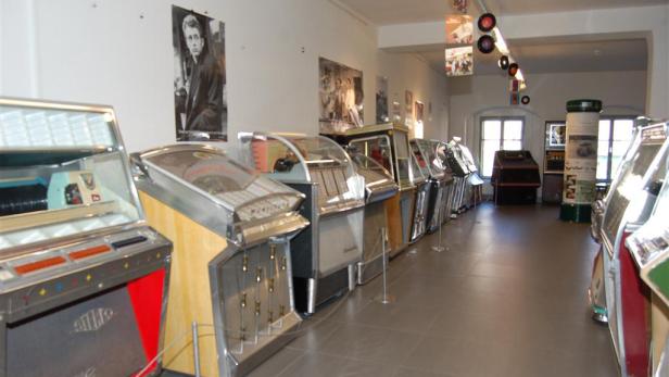 Eine Reihe von Jukeboxen in einem Museum, mit einem Poster von James Dean an der Wand.