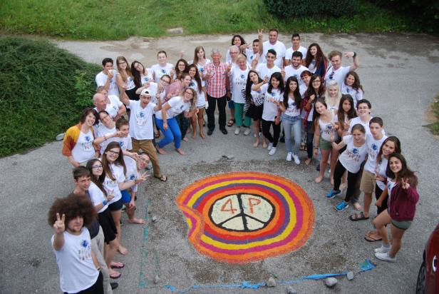 Eine Gruppe junger Leute steht um ein buntes Friedenssymbol auf dem Boden.