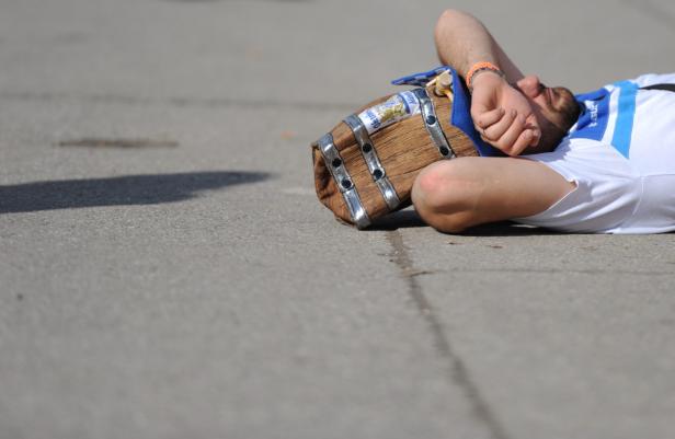 Ein Mann liegt mit einem kleinen Bierfass auf dem Asphalt.