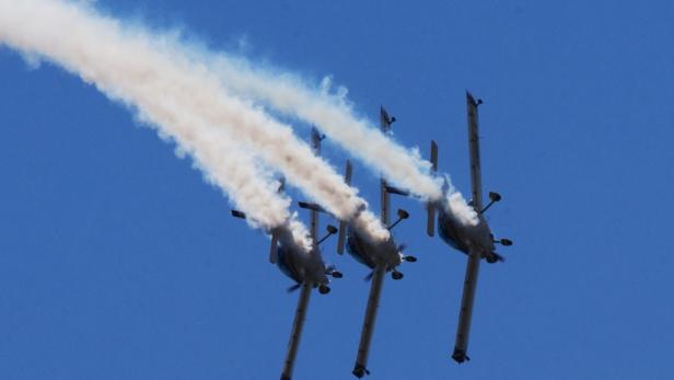 Drei Flugzeuge fliegen in Formation und hinterlassen Rauchspuren am blauen Himmel.
