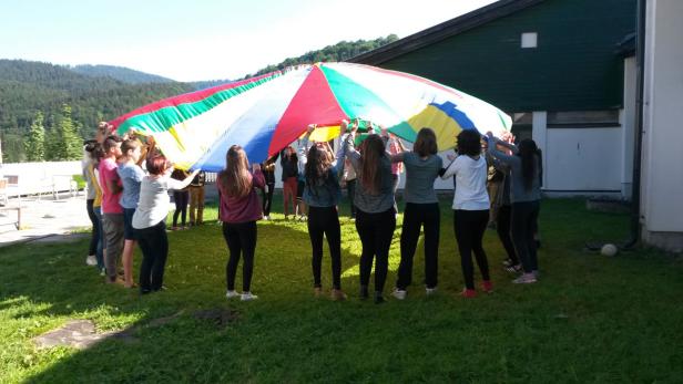 Eine Gruppe von Menschen hält einen bunten Schwungtuch im Freien hoch.