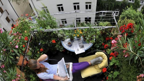 Eine Frau liest Zeitung auf einem üppig bepflanzten Balkon.