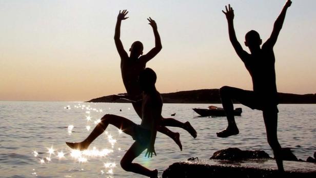 Drei Kinder springen bei Sonnenuntergang ins Meer.