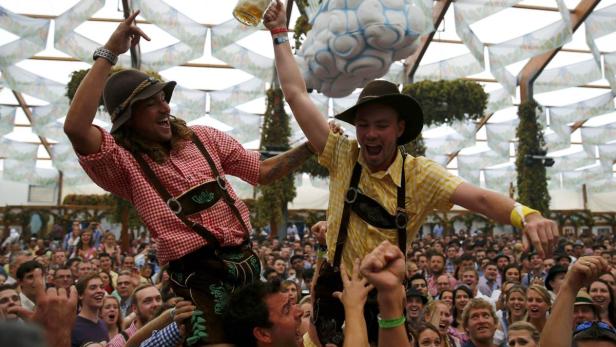 Zwei Männer in Tracht werden auf den Schultern getragen und feiern mit Bier auf dem Oktoberfest.