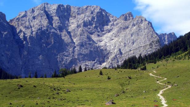 Ein Wanderweg schlängelt sich vor einer beeindruckenden Bergkulisse entlang.