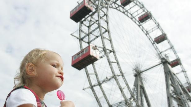 Ein kleines Mädchen isst einen Lutscher vor dem Wiener Riesenrad.