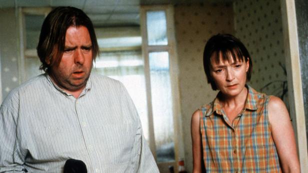 Ein Mann und eine Frau stehen in einem Raum mit gemusterter Tapete.