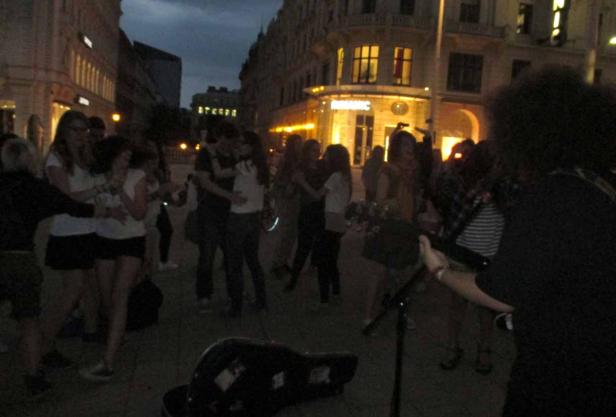 Eine Gruppe von Menschen tanzt abends auf einer belebten Straße zu Live-Musik.
