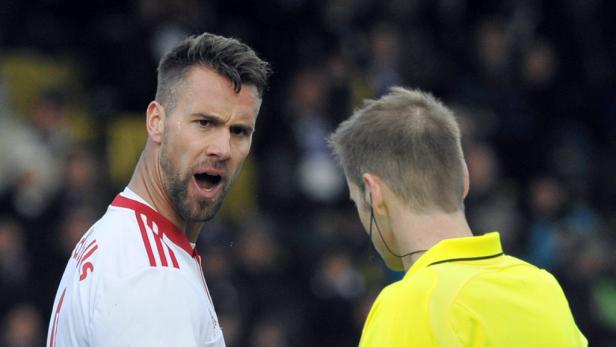 Ein Fußballspieler diskutiert aufgeregt mit einem Schiedsrichter.