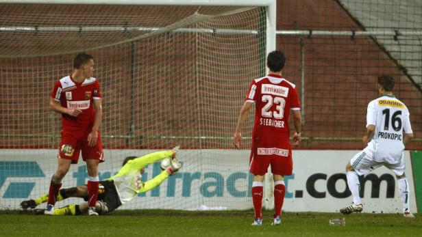 Ein Fußballspieler schießt auf das Tor, während der Torwart versucht, den Ball abzuwehren.