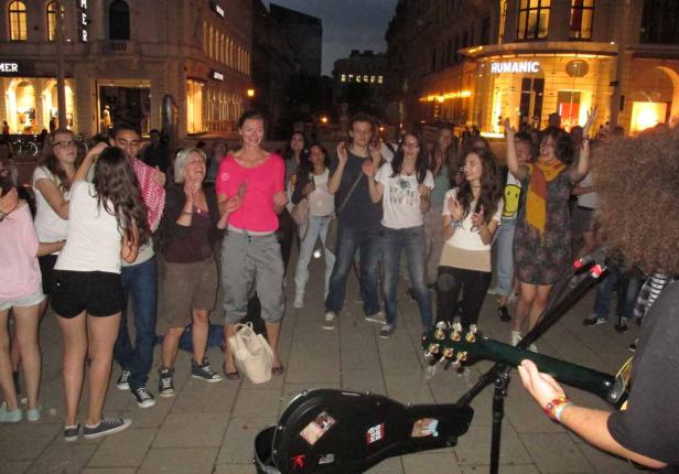 Eine Gruppe von Menschen tanzt und klatscht zu einem Straßenmusiker in der Stadt.