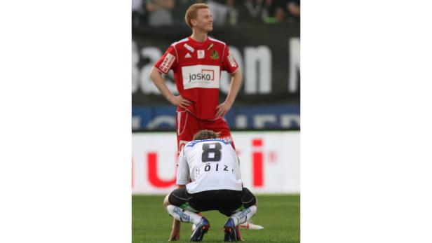 Ein Fußballspieler steht enttäuscht vor einem anderen, der auf dem Feld hockt.