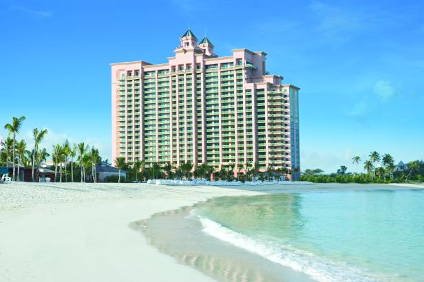 Ein großes, rosafarbenes Hotel steht an einem weißen Sandstrand mit Palmen.