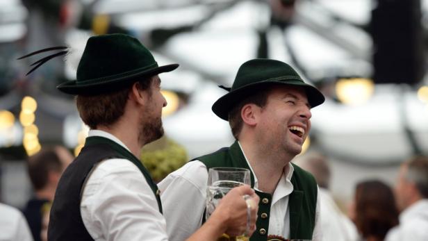 Zwei Männer in Trachtenhüten und -westen lachen und halten Bierkrüge.