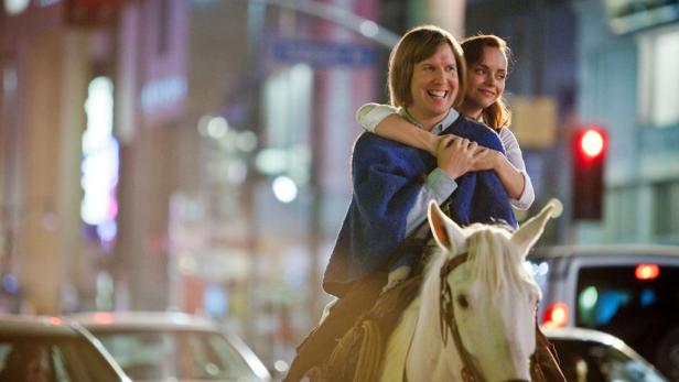 Pete Holmes und Christina Ricci reiten auf einem weißen Pferd durch eine belebte Stadt.