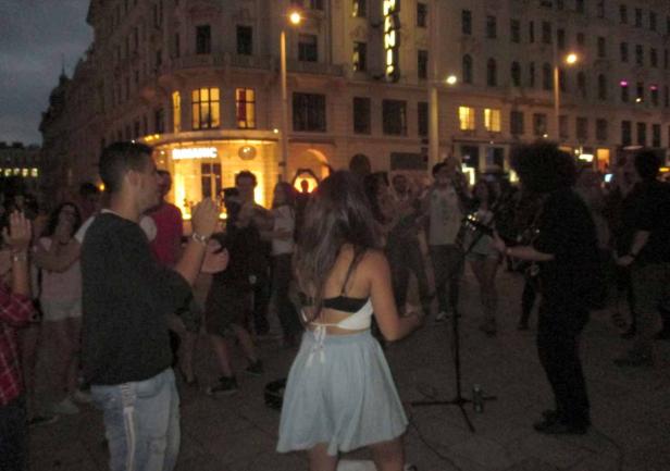 Eine Menschenmenge tanzt zu Live-Musik auf einer belebten Straße.