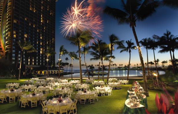 Ein festlich gedeckter Tisch unter Palmen mit Feuerwerk am Abend.