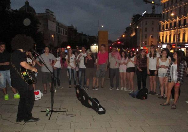 Ein Straßenmusiker spielt Gitarre für eine Gruppe junger Leute in einer Stadt.