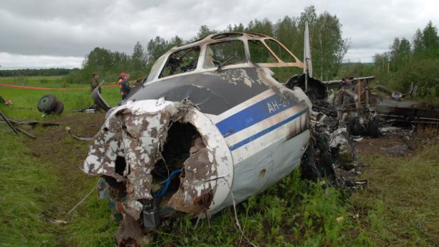 Das Wrack eines AH-26 Flugzeugs liegt auf einem Feld.