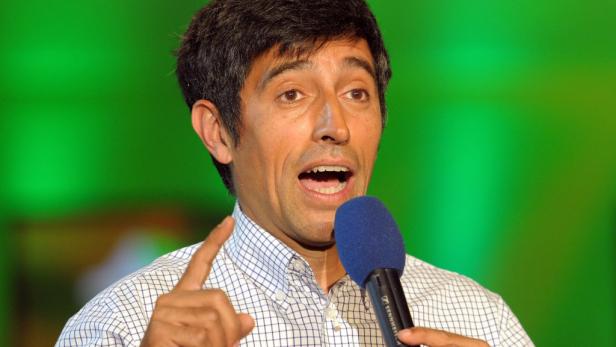 Ein Mann spricht mit einem Mikrofon in der Hand und gestikuliert mit dem Finger.