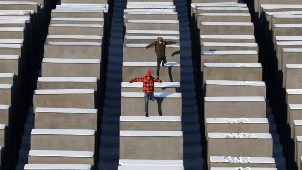 Zwei Personen springen auf den schneebedeckten Stelen des Holocaust-Mahnmals in Berlin.