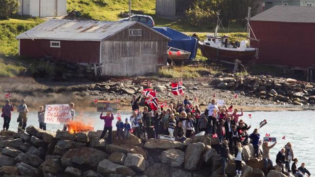 Eine Menschenmenge mit norwegischen Flaggen demonstriert am Wasser, während ein Feuer brennt.