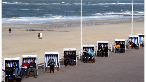 Menschen sitzen in Strandkörben an einem sonnigen Strand.