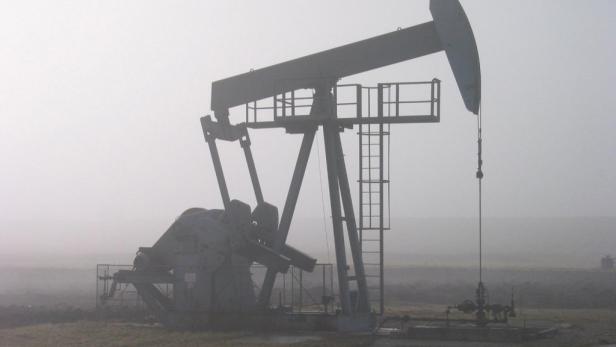 Eine Ölförderanlage steht im Nebel auf einem Feld.